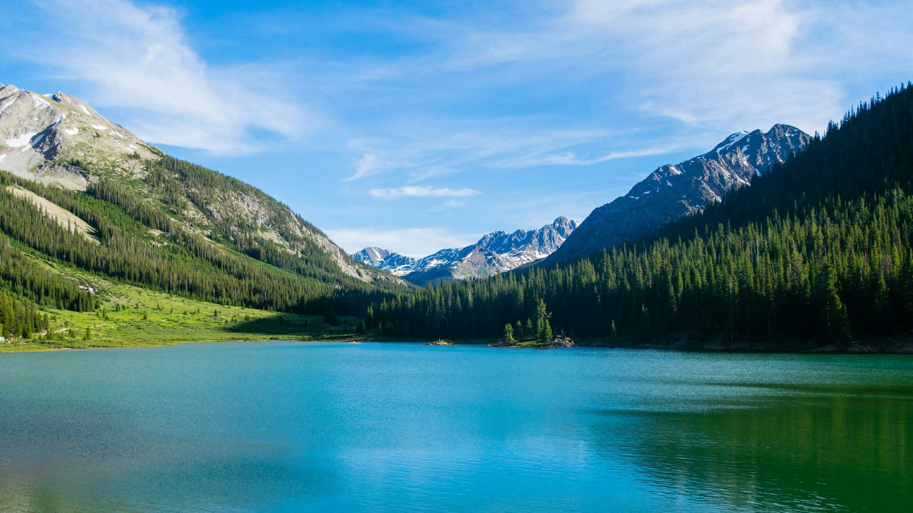 A Colorado alpine lake beneath mountain peaks and a wide blue sky